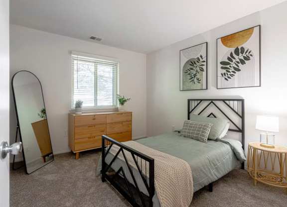 A bedroom with a bed, dresser, mirror, and lamp.