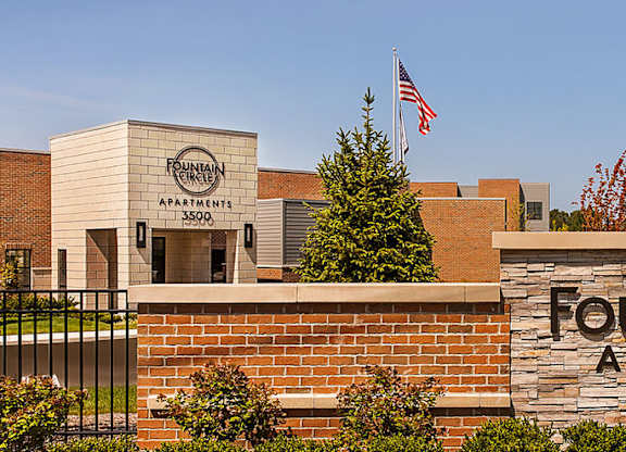 The image shows the front of Fountain Circle Apartments with a sign and a flag.