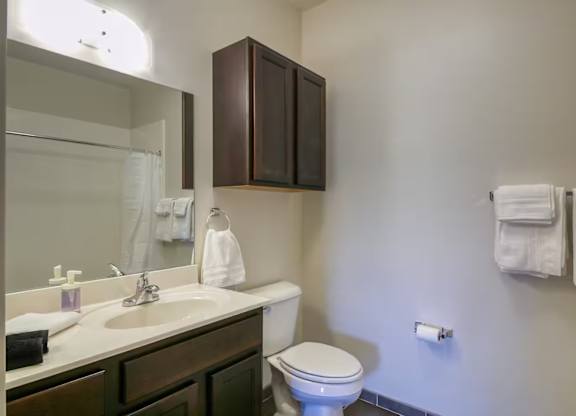 A white toilet sits in a bathroom with a white sink and brown cabinets.