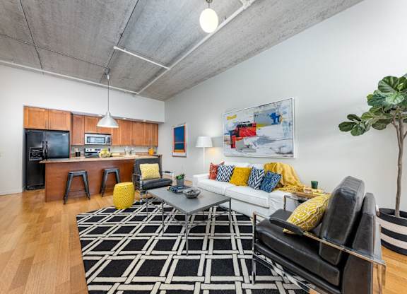 A living room with a black and white rug, a black couch, and a yellow pouf.