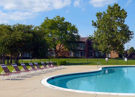 A pool surrounded by lawn chairs and trees.