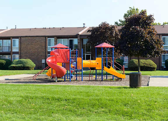 A playground with a red slide and yellow slide in front of a building.