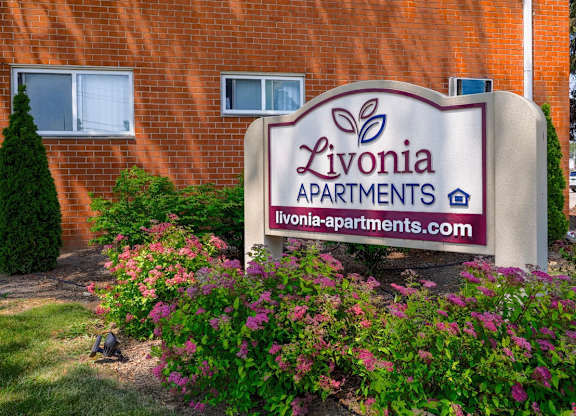 A sign for Livonia Apartments is displayed in front of a brick building.