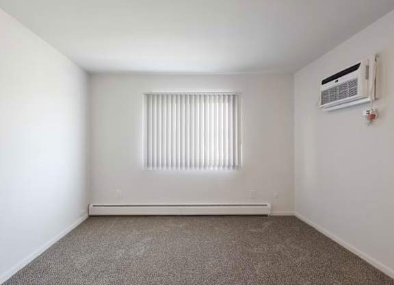 A room with a window covered by blinds and an air conditioner on the wall.