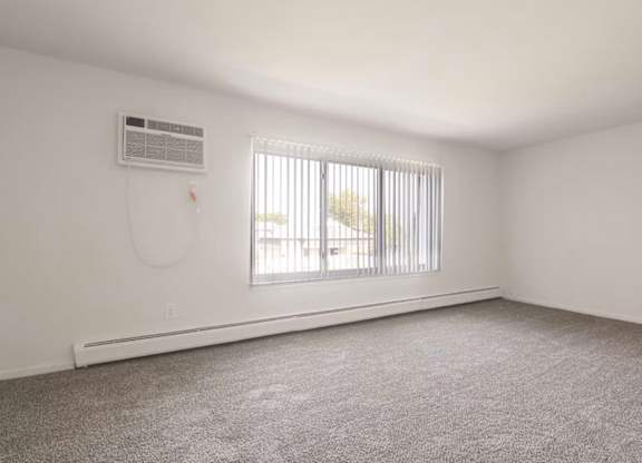 A room with a window covered by blinds and an air conditioner on the wall.