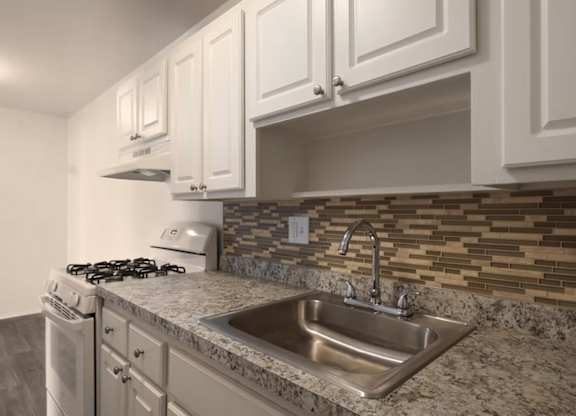 A kitchen with a stove, sink, and cabinets.