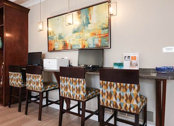 A painting hangs on the wall above a kitchen island with three chairs with patterned upholstery.