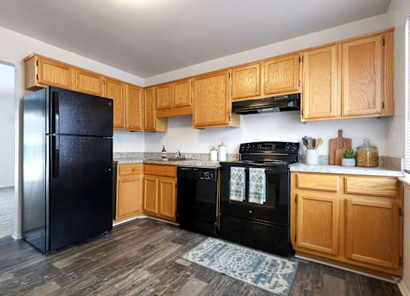 A black refrigerator stands in a kitchen with wooden cabinets and a black stove.