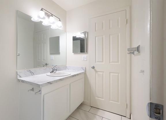A white bathroom with a sink, mirror, and lighting fixture.