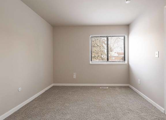 A room with a carpeted floor and a window with blinds.