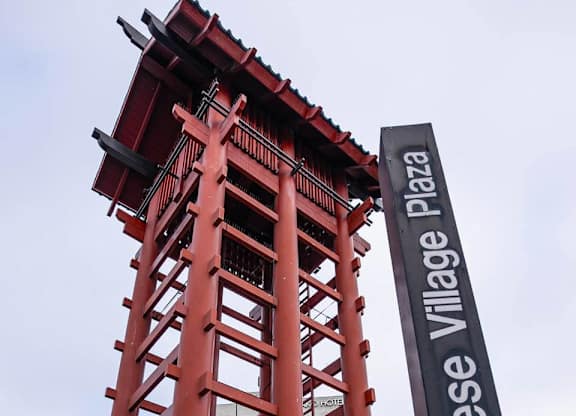 A red and black Japanese pagoda-style structure stands in front of a sign that reads "Japanese Village Plaza.".