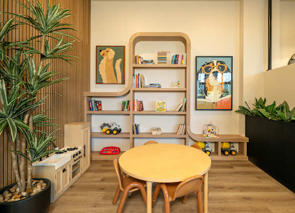 A room with a round table, a potted plant, and a bookshelf with books and picture frames.