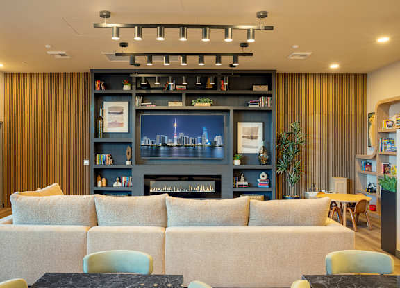 A room with a large couch, a coffee table, and a bookshelf with a cityscape picture on it.