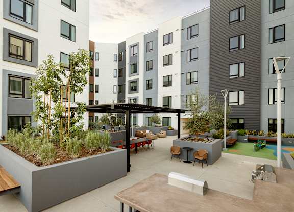 A modern courtyard with a bench, a table and a tree.