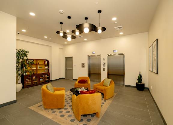 A spacious lobby with a carpeted floor, yellow chairs, and a potted plant.
