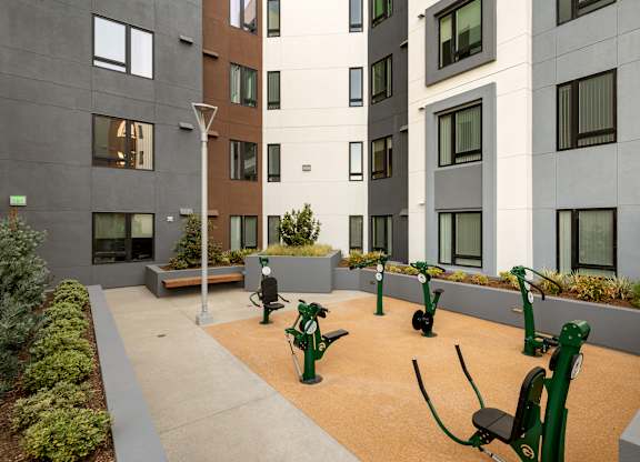 A modern courtyard with exercise equipment and buildings in the background.