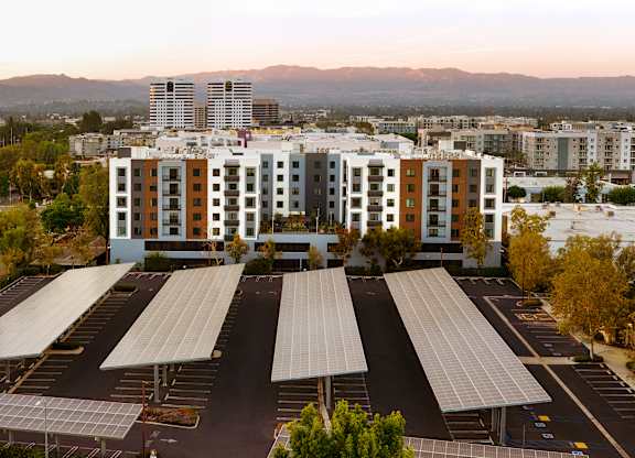 A parking lot with solar panels and apartment buildings in the background.