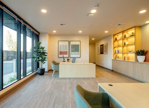 A modern office space with a reception desk, chairs, and a large window.