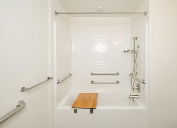 A white bathroom with a wooden seat in the middle of the tub.