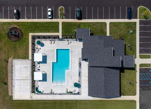 A swimming pool is surrounded by a tennis court and a building.