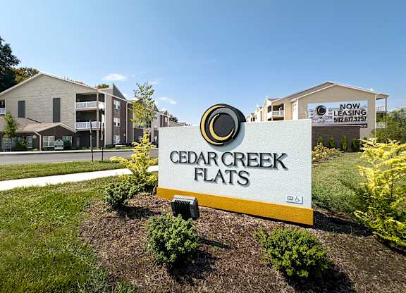 A sign for Cedar Creek Flats in front of apartment buildings.