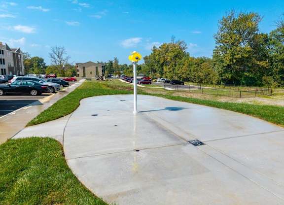 A yellow sign on a pole stands in the middle of a concrete area with cars parked in the background.