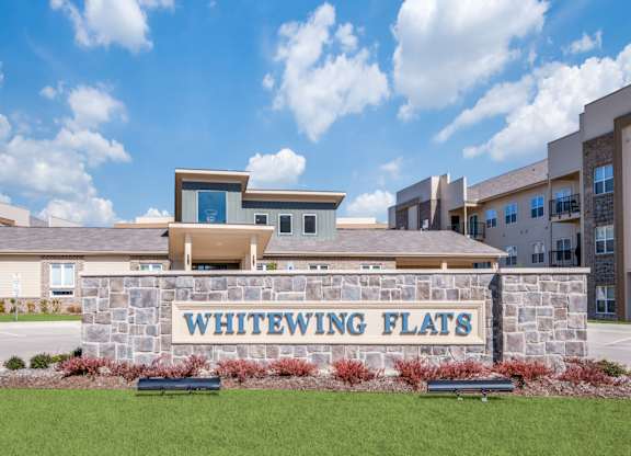 Whitewing Flats is a residential complex with a stone wall and a sign in front.