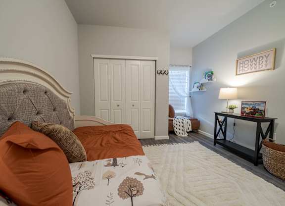 A bedroom with a large bed and a small table with a lamp.