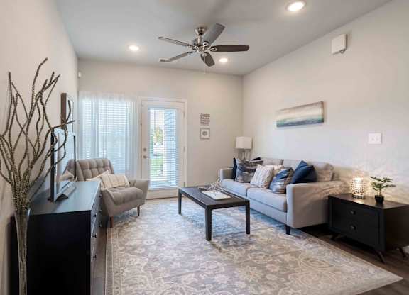 A living room with a grey couch, a black side table, and a ceiling fan.