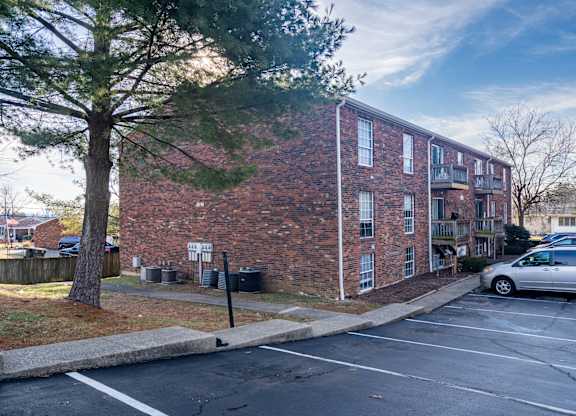 A parking lot in front of a brick building with a tree on the left.