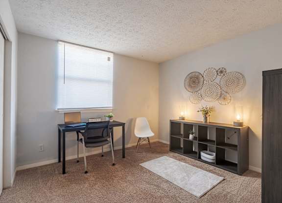 A room with a desk, chair, and shelves with decorative items.
