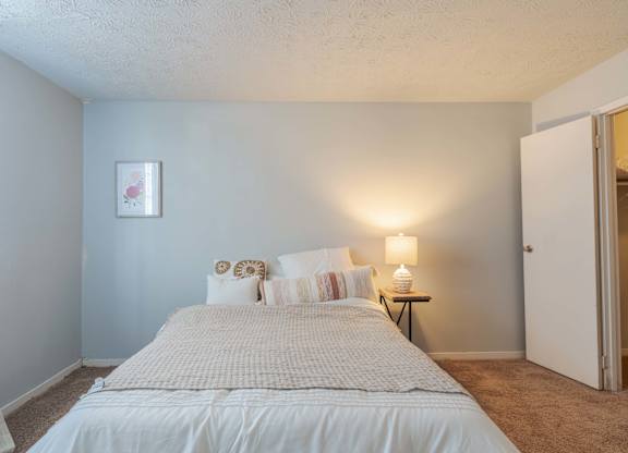 A bedroom with a bed, pillows, a nightstand, and a lamp.