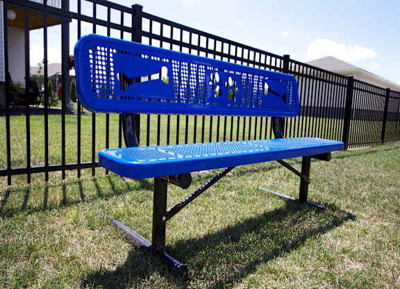 a blue bench in the grass in front of a fence