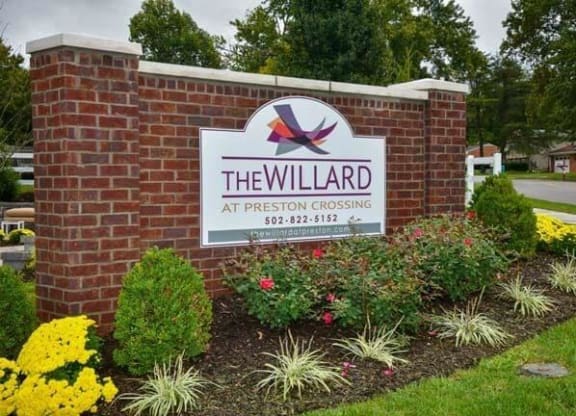 a sign for the willard at prestons crossing in front of a garden