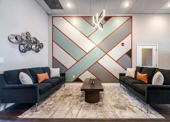 A living room with two black couches and a coffee table in front of a wall with a red and white geometric design.