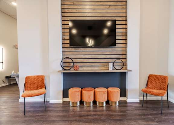 Two orange chairs are placed in front of a fireplace with a TV above it.