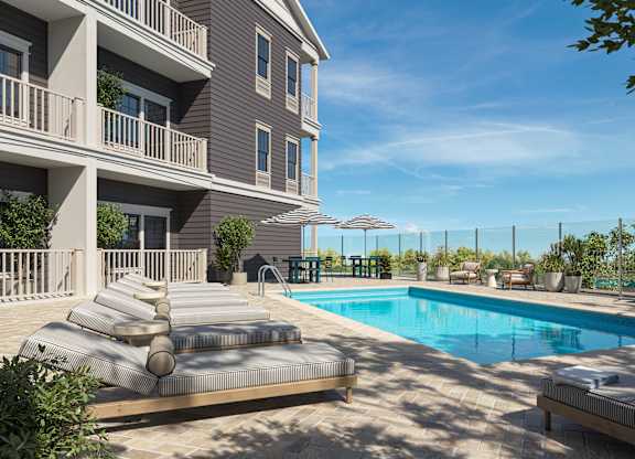 A large swimming pool is surrounded by a sun lounger and a building.