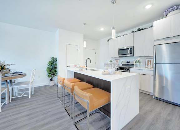 a kitchen with stainless steel appliances and a bar with orange stools at The Franklin at Hillsborough Apartments, New Jersey, 08844