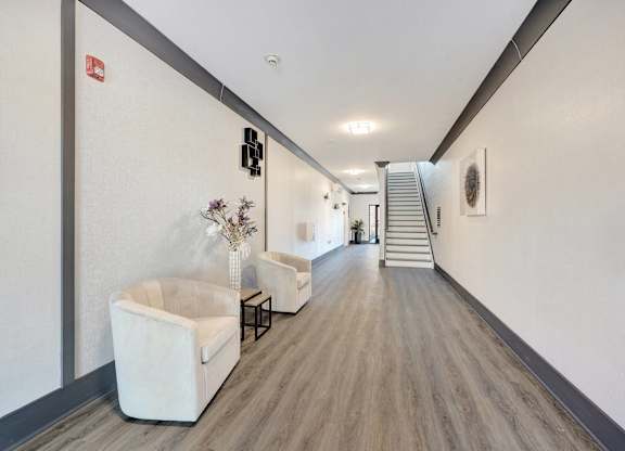 a long hallway with white walls and chairs and a staircase at The Franklin at Hillsborough Apartments, Hillsborough, NJ
