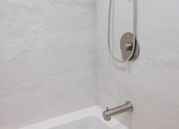 a shower in a white bathroom with white tiles