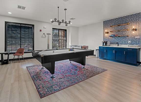 A pool table is in the middle of a room with a rug on the floor.