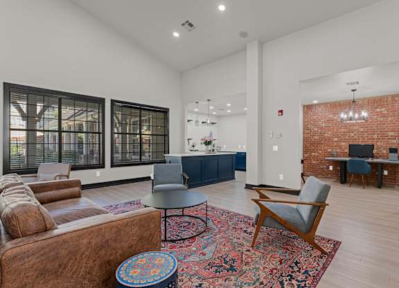A living room with a brown leather couch, a grey armchair, a round table, and a red and blue ottoman.