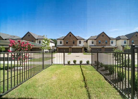 A black metal fence surrounds a green lawn in front of a row of houses.