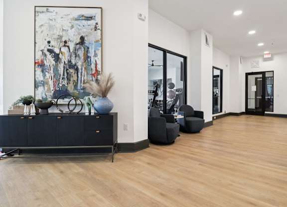 A large abstract painting hangs on a white wall above a black cabinet with a vase and a blue ball on top.
