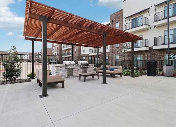 A wooden pergola is over a concrete patio with benches.
