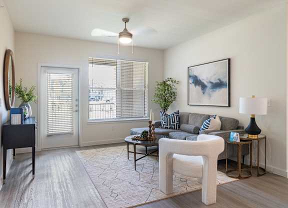 A living room with a grey couch, a white chair, and a painting on the wall.