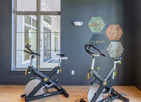 Two exercise bikes are in a room with a window.