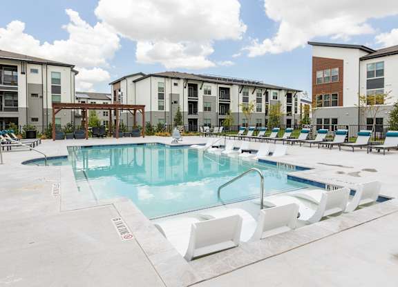 A swimming pool with lounge chairs in front of apartment buildings.