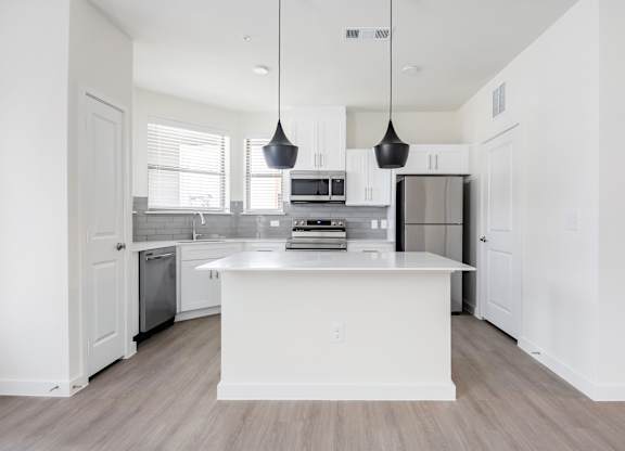 A modern kitchen with a white island and pendant lights.