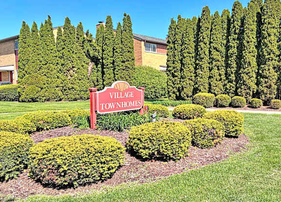 A sign that says Village Townhomes in front of a row of trees.